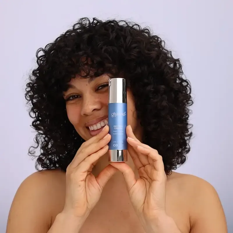 Smiling woman with curly hair holding a blue and silver skincare product.