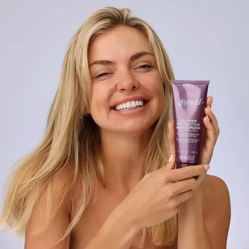 Smiling woman with blonde hair holding a purple product tube, promoting skincare.